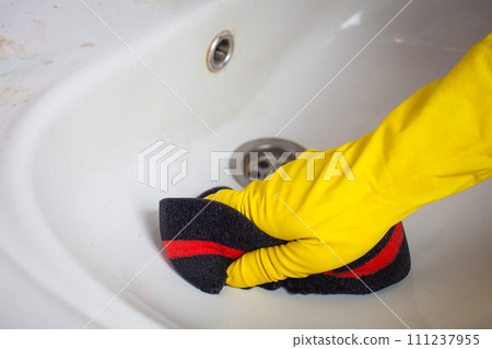 Maid with rubber glove cleaning tap and sink. 111237955