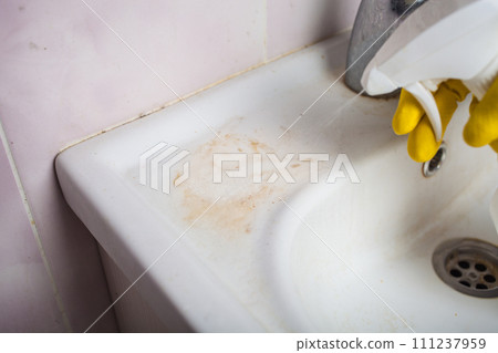 Maid with rubber glove cleaning tap and sink. 111237959