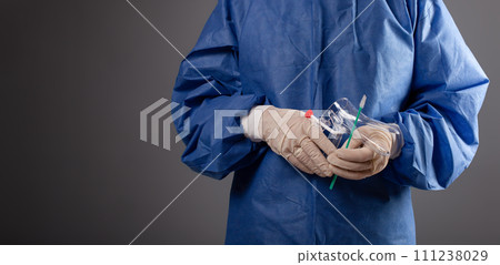 A gynecologist with a venus mirror in his hands. Gynecological accessories, brush, stick. A doctor in a medical mask, a robe, gloves, with a gynecological mirror on a gray background. 111238029
