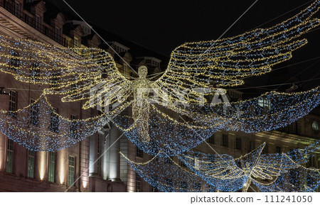 Flying angel Christmas decoration led lights display. Dramatic view of the traditional Christmas decoration lights hanging above Regent Street during dusk. Flying angel Christmas decoration led lights display. Dramatic view of the traditional Christmas decoration lights hanging above Regent Street during dusk. 111241050
