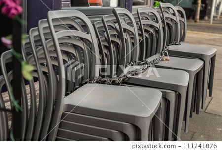 Pile of stacking silver gray plastic chairs are beside of The cafe terrace at sunny day. Pile of stacking silver gray plastic chairs are beside of The cafe terrace at sunny day. 111241076