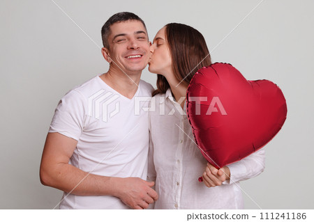 Romantic man and woman holding heart shaped air balloon and kissing happy joyful family love couple celebrating Valentine's Day expressing love and warm feelings Romantic man and woman holding heart shaped air balloon and kissing happy joyful family love couple celebrating Valentine's Day expressing love and warm feelings 111241186