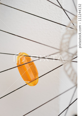 Abstract View of a Yellow Bicycle Reflector Between Spokes Against a White Wall 111244132