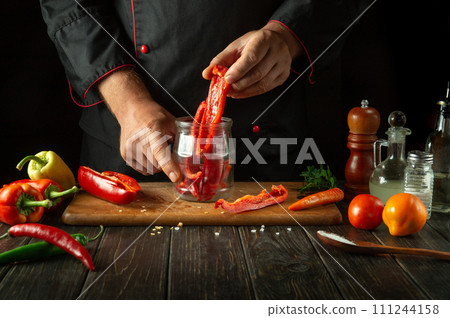 The cook preparing fresh vegetables in the kitchen. The chef puts fresh peppers in a jar in the kitchen. Healthy or vegetarian food concept 111244158