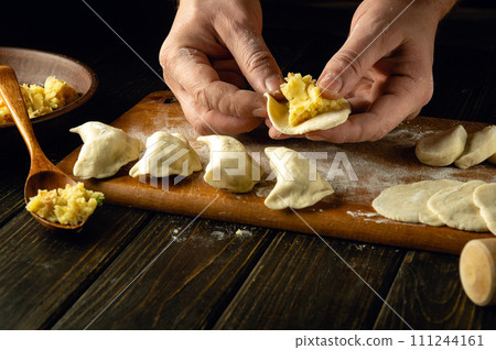 Close-up of a man's hands making a dumpling from dough. The concept of cooking dumplings with potatoes on the kitchen table. Ukrainian traditional cuisine 111244161