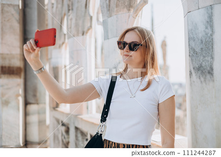 Beautiful woman taking selfie on Roof of Milan Cathedral Duomo di Milano, Italy. Traveling Europe in summer. Attractive female is exploring city, tourist makes photo or video on smartphone Beautiful woman taking selfie on Roof of Milan Cathedral Duomo di Milano, Italy. Traveling Europe in summer. Attractive female is exploring city, tourist makes photo or video on smartphone 111244287