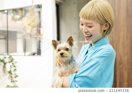 Short-haired woman holding a Yorkshire terrier at a dog salon 111245156