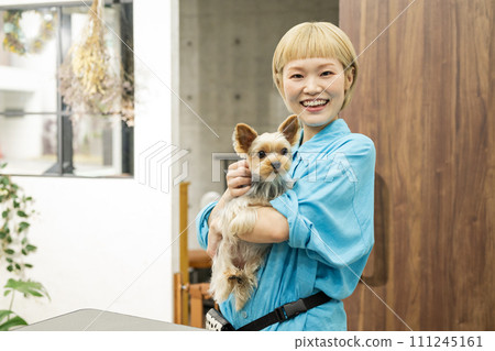 Short-haired woman holding a Yorkshire terrier at a dog salon 111245161