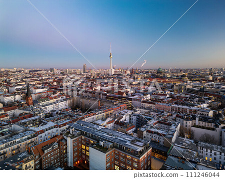 Aerial panoramic shot of apartment houses in Mitte district at twilight. Popular tall Fernsehturm in distance against clear sky. Berlin, Germany 111246044