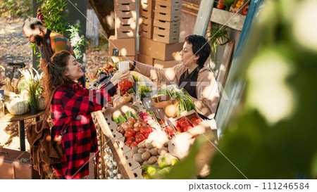 Female client and vendor drinking cup of hot coffee at farmers market, woman buying fresh eco fruits and veggies. Small business owner selling produce and enjoying visit from regular customer. Female client and vendor drinking cup of hot coffee at farmers market, woman buying fresh eco fruits and veggies. Small business owner selling produce and enjoying visit from regular customer. 111246584