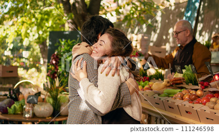 Woman vendor greeting regular client and hugging at farmers market stand, being happy selling locally grown products. Positive farmer sharing hug with customer, enjoying visit at street festival. Woman vendor greeting regular client and hugging at farmers market stand, being happy selling locally grown products. Positive farmer sharing hug with customer, enjoying visit at street festival. 111246598