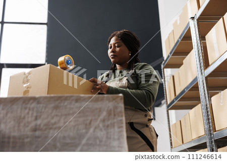 African american worker taping customers orders using adhesive tape in storehouse, preparing packages for delivery. Storage room employee working at merchandise quality control in warehouse African american worker taping customers orders using adhesive tape in storehouse, preparing packages for delivery. Storage room employee working at merchandise quality control in warehouse 111246614