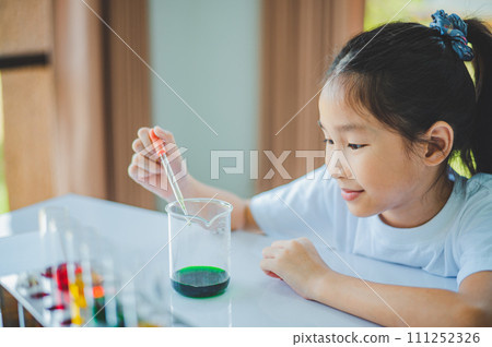 little scientist looking through a microscope and test tubes filled with chemicals for learning about science and experiments. little scientist looking through a microscope and test tubes filled with chemicals for learning about science and experiments. 111252326