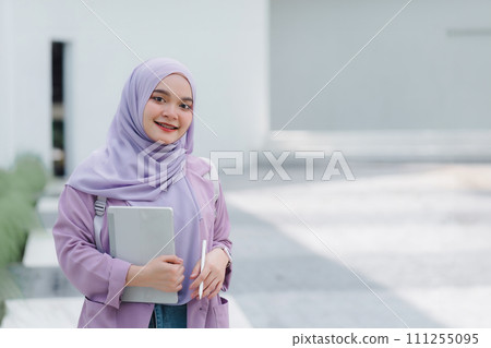 Muslim university student holding a tablet while standing outdoors on campus. Muslim university student holding a tablet while standing outdoors on campus. 111255095