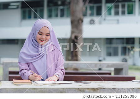 Asian Muslim university student doing homework alone outdoors on campus. 111255096