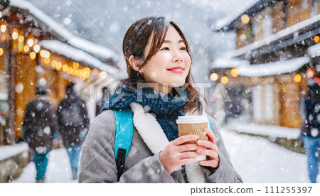 A female traveler strolls through the falling snow with coffee in hand A female traveler strolls through the falling snow with coffee in hand 111255397