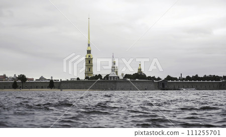 Close up of small waves of neva river and the golden spire of the Peter and Paul fortress. Action. Cloudy sky above the Petropavlovskaya fortress and Neva river. Close up of small waves of neva river and the golden spire of the Peter and Paul fortress. Action. Cloudy sky above the Petropavlovskaya fortress and Neva river. 111255701
