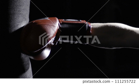 Fighter Practicing Some Kicks With Punching Bag - A Man With A Tattoo Boxing On dark Background. Kick, punching bag on dark background. Black punching bag weighs at the gym Fighter Practicing Some Kicks With Punching Bag - A Man With A Tattoo Boxing On dark Background. Kick, punching bag on dark background. Black punching bag weighs at the gym 111255722