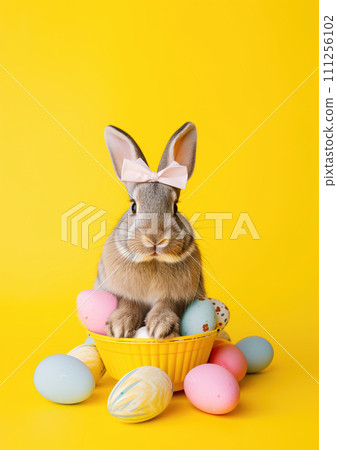 Holiday easter rabbit with bow sitting on colored decorated easter eggs on neutral yellow background Holiday easter rabbit with bow sitting on colored decorated easter eggs on neutral yellow background 111256102
