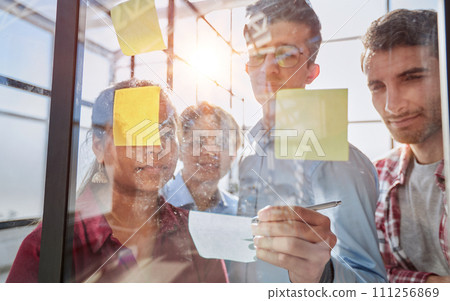 A group of business people behind a glass wall in the office sticking notes 111256869