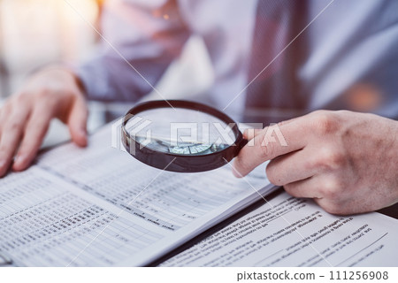 Businessman looking through a magnifying glass to documents Businessman looking through a magnifying glass to documents 111256908