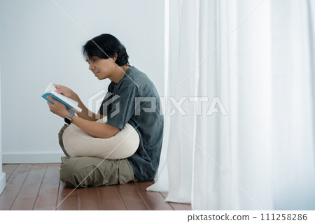 wellness and wellbeing concept with asian man sit and relax and read in livingroom wellness and wellbeing concept with asian man sit and relax and read in livingroom 111258286