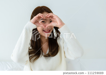 Front view of cute young Asian woman smiling and looking at camera with hands showing heart shape 111259089