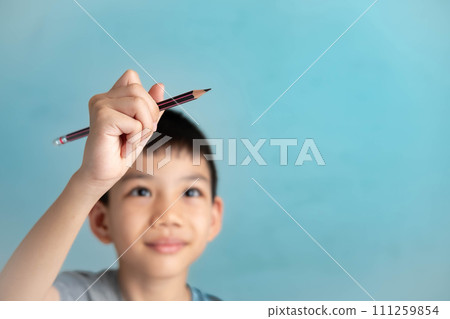 Asian boy holding a pencil drawing in the air, imagination concept of a child on a blue background Asian boy holding a pencil drawing in the air, imagination concept of a child on a blue background 111259854