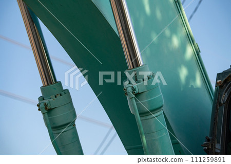 Closeup view of stainless steel hydraulic arm on green excavator. Stainless steel power in the hydraulic arm of an excavator. Stainless steel hydraulic arm of excavator unveils industrial precision. 111259891