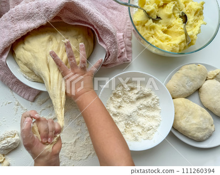 The hands of child knead the dough for making pies on white table, top view. 111260394