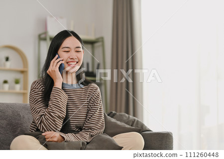 Pretty young woman enjoying pleasant mobile conversation sitting on couch at home Pretty young woman enjoying pleasant mobile conversation sitting on couch at home 111260448