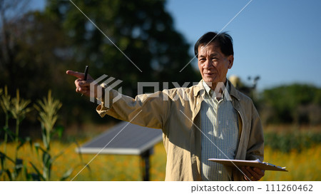 Mature farmer standing front of solar panels in a smart agricultural farm. Renewable energy and agriculture concept Mature farmer standing front of solar panels in a smart agricultural farm. Renewable energy and agriculture concept 111260462