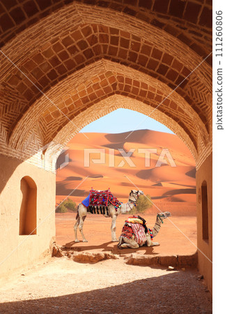 Ancient arch at entrance to desert. View of sand dunes through stone arch. Travel, resort, vacation and holiday concept. Beautiful desert landscape with sand dunes and camels in a colorful horse-cloth 111260806