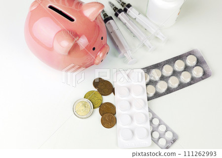 The blue piggy bank is surrounded by various medicines and euro coins 111262993