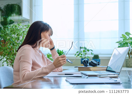 Tired sad mature woman at workplace at table with computer laptop Tired sad mature woman at workplace at table with computer laptop 111263773