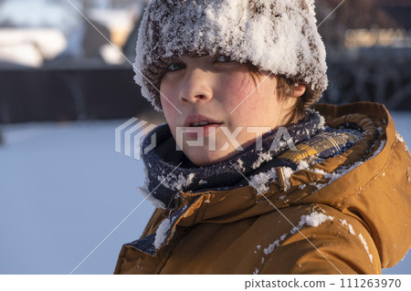 Portrait of a cute teenage boy, playing in snow, in a snow-covered hat in winter. Wet skin Portrait of a cute teenage boy, playing in snow, in a snow-covered hat in winter. Wet skin 111263970