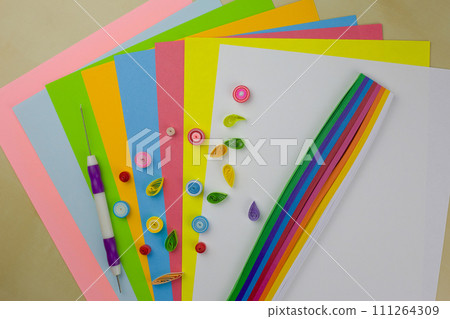 Quilling technique. Rolled colored paper for decoration on a table with paper strips. Develop fine motor skills with paper and a special hobby tool Quilling technique. Rolled colored paper for decoration on a table with paper strips. Develop fine motor skills with paper and a special hobby tool 111264309