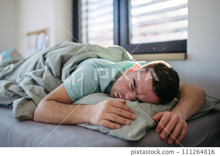 Young man with down syndrome sleeping in his bed. Lying on abdomen, resting in bedroom. Young man with down syndrome sleeping in his bed. Lying on abdomen, resting in bedroom. 111264816