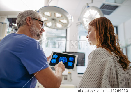 Doctor showing teenage patient MRI scan on tablet, discussing test result in emergency room. Doctor showing teenage patient MRI scan on tablet, discussing test result in emergency room. 111264910