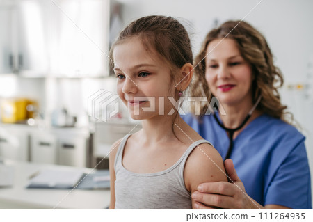 Orthopedist examines the spine, posture, and spinal deformities of little girl. Girl visiting paediatrician for annual preventive exam. Concept of preventive health care for children. 111264935