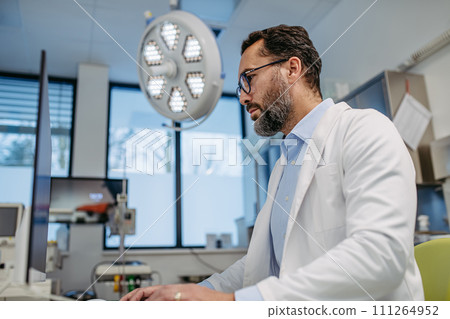 Portrait of ER doctor in hospital working in emergency room. Healthcare worker looking at MRI scan on medical computer in emergency room. 111264952