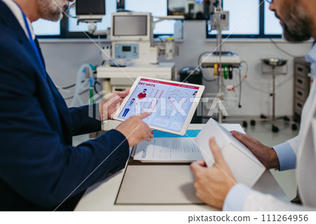 Pharmaceutical sales representative presenting new medication to doctor in medical building, holding box with medication samples. 111264956
