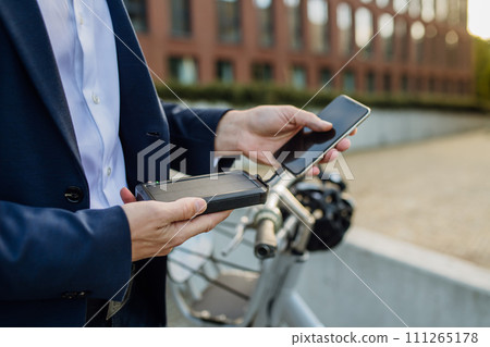 Businessman, freelancer or manager working outdoors in city park. Charging smartphone with solar phone charger. Concept of working remotely. 111265178