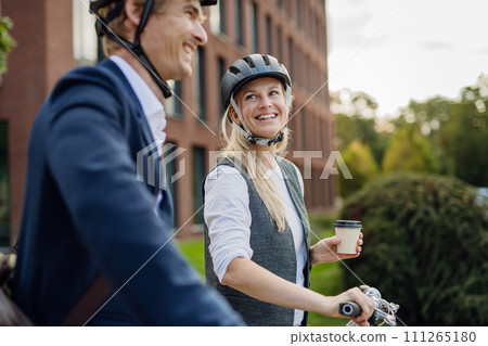 Spouses commuting through the city, talking and walking by bike on street. Middle-aged city commuters traveling from work by bike after a long workday. Spouses commuting through the city, talking and walking by bike on street. Middle-aged city commuters traveling from work by bike after a long workday. 111265180