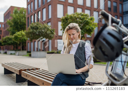 Businesswoman, freelancer or manager working outdoors in city park. Woman with laptop on knees sitting on park bench during sunny day. Concept of working remotely. 111265183