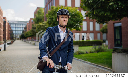 Handsome middle-aged man commuting through the city by bike in suit. Male city commuter traveling from work by bike after a long workday. 111265187