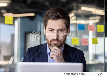 Serious concentrated thinking financier businessman at workplace preparing electronic financial report, mature experienced man in business suit typing laptop keyboard, reading report, inside office. 111265353