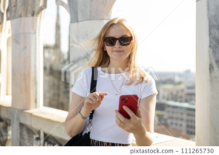 30s woman tourist checks her smartphone. Use technology concept, Traveling Europe in summer. A Roof of Milan Cathedral Duomo di Milano, Italy 111265730