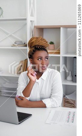 Distance work. Remote workplace. Pensive positive woman thinking about project considering new ideas sitting light office workplace. Distance work. Remote workplace. Pensive positive woman thinking about project considering new ideas sitting light office workplace. 111265869