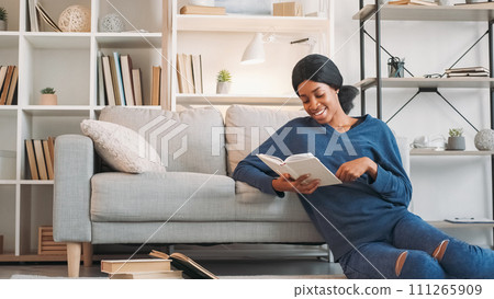 Literature lifestyle. Favorite book. Young relaxed happy woman enjoying reading interesting novel story on floor at comfy sofa at home in living room free space. 111265909